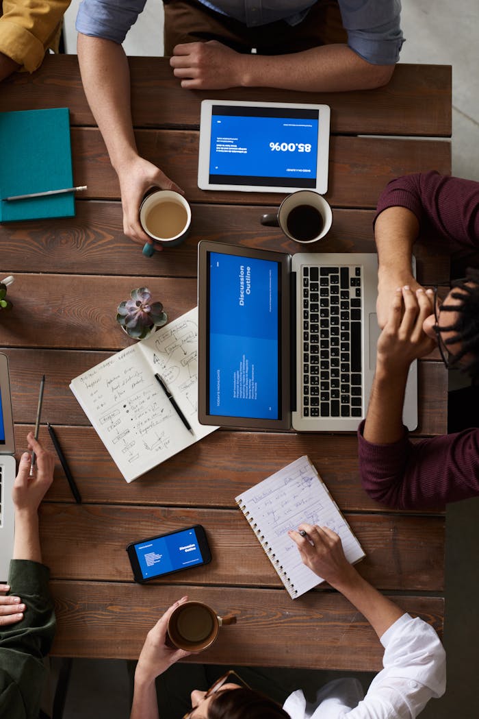 Contact Group of coworkers discussing business strategies with laptops and tablets in a modern office setting.